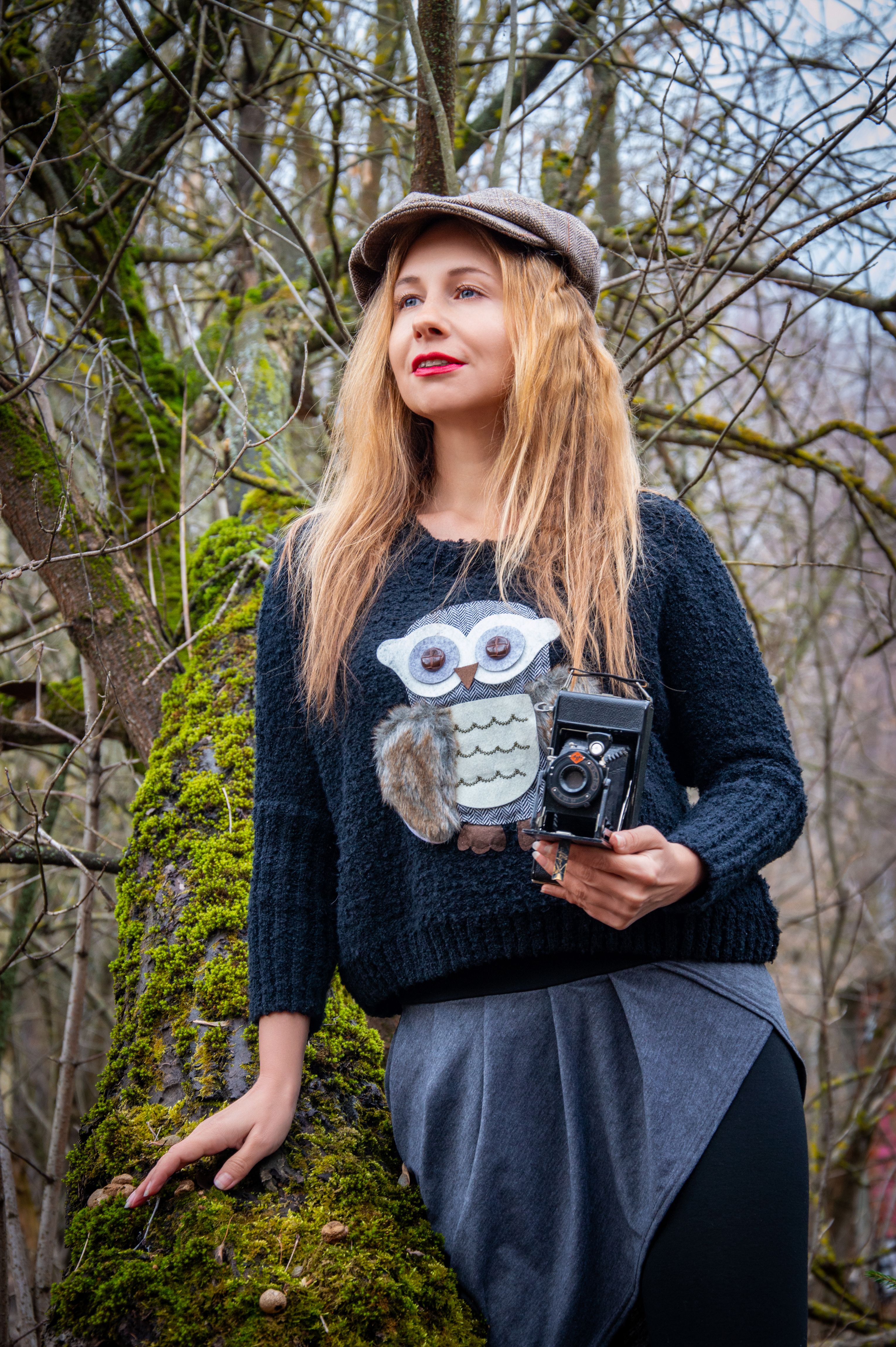 Young woman in stylish outfit holding a vintage camera outdoors.