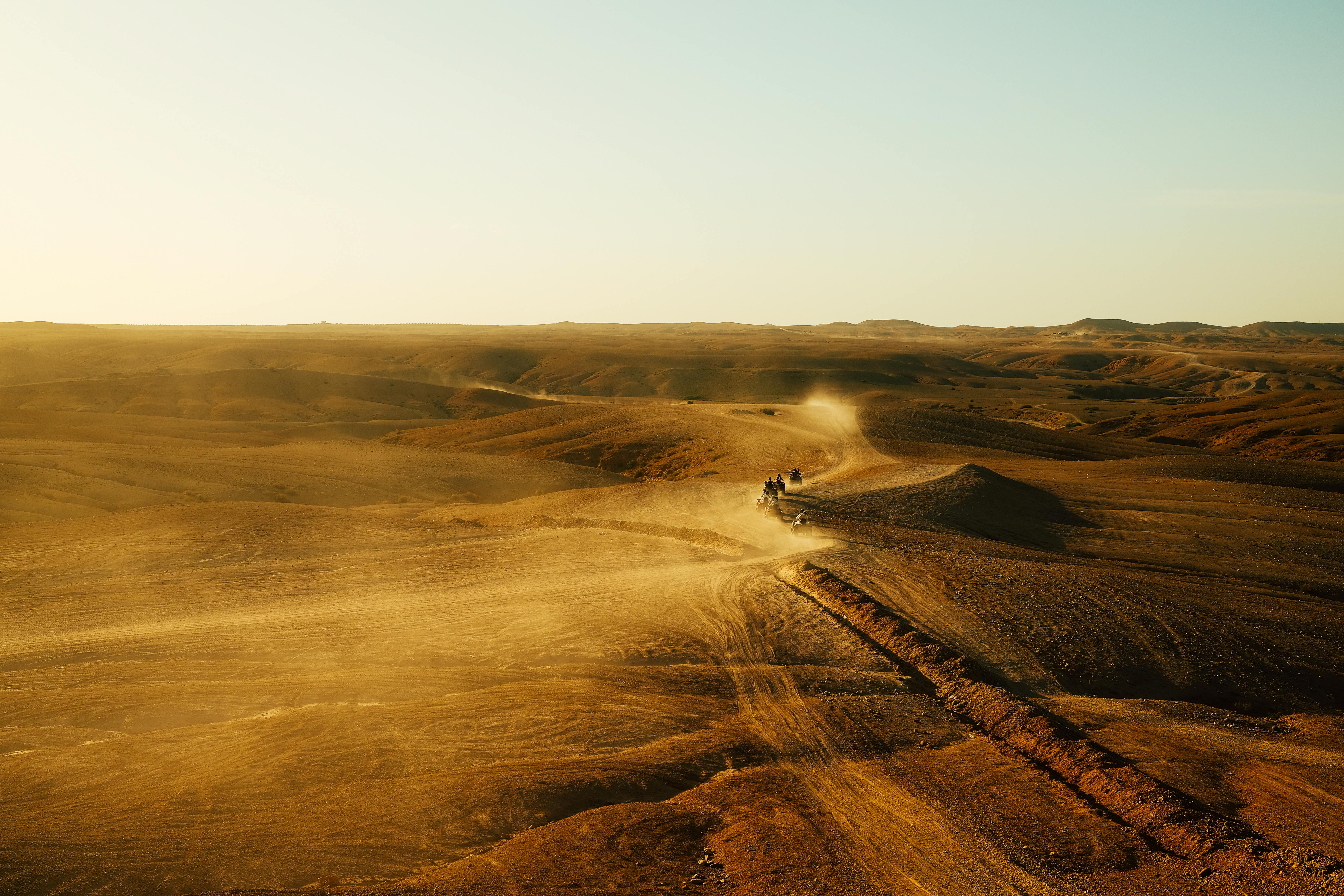 Desert expedition with all-terrain vehicles traversing expansive dunes under a clear sky.