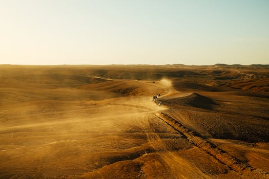 Desert expedition with all-terrain vehicles traversing expansive dunes under a clear sky.