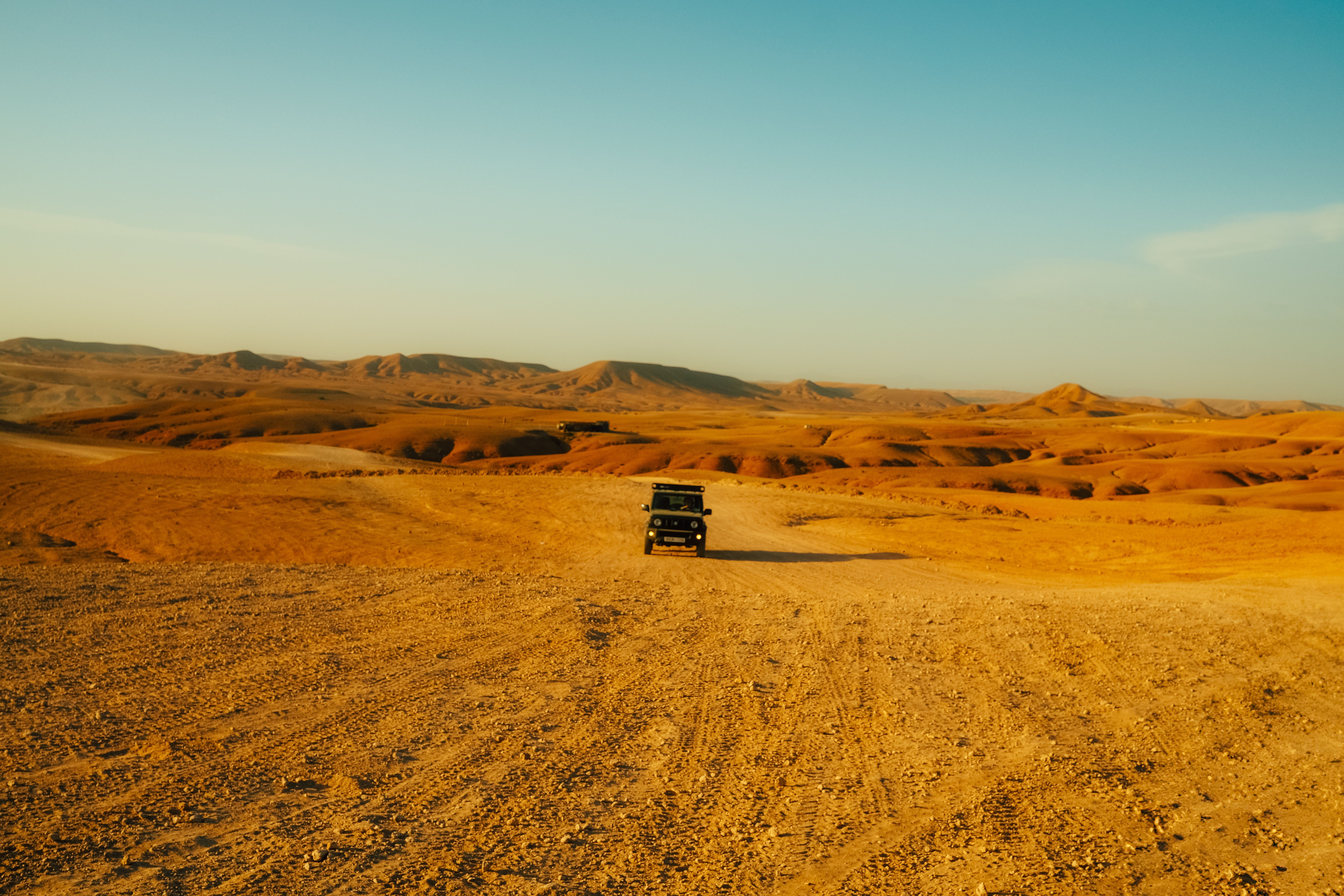 An off-road vehicle traverses a vast desert landscape under a clear blue sky, showcasing adventure travel.