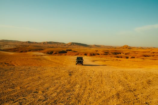 An off-road vehicle traverses a vast desert landscape under a clear blue sky, showcasing adventure travel.