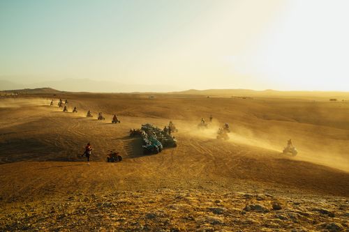 Free Group of people riding quad bikes across a vast, sandy desert terrain at sunset. Stock Photo