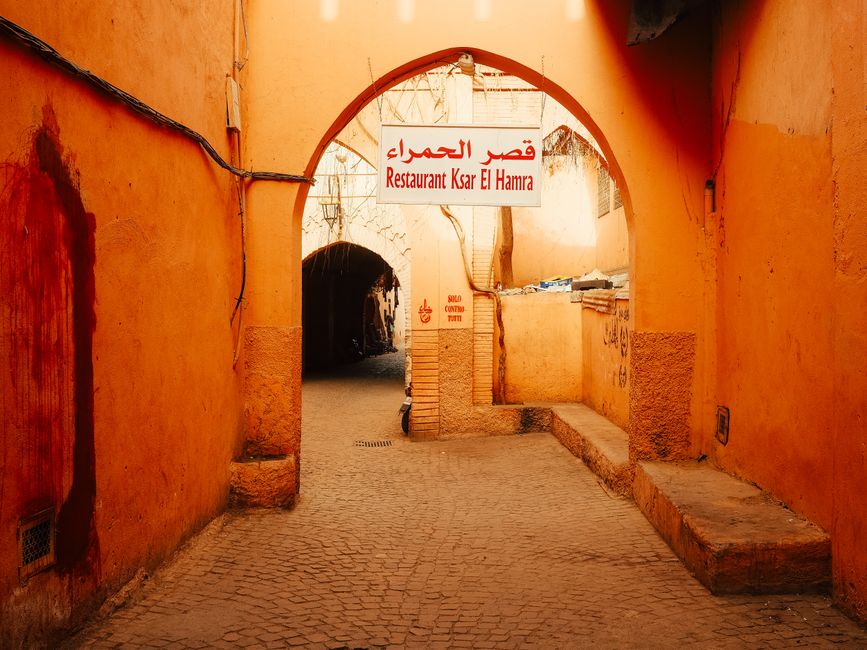 Explore a vibrant alleyway in Marrakesh featuring a traditional Moroccan archway and local restaurant sign.
