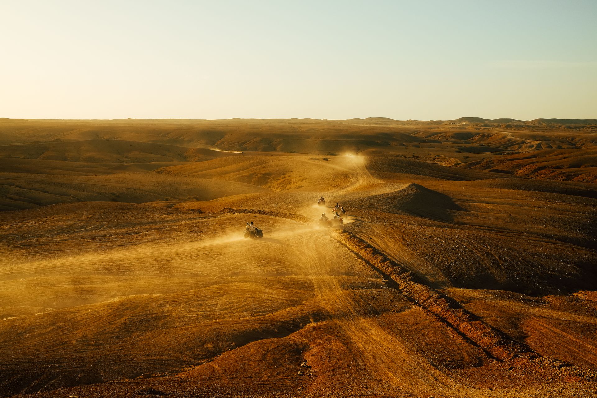 ATVs speed across a vast desert landscape during a stunning sunset, creating a thrilling sense of adventure.