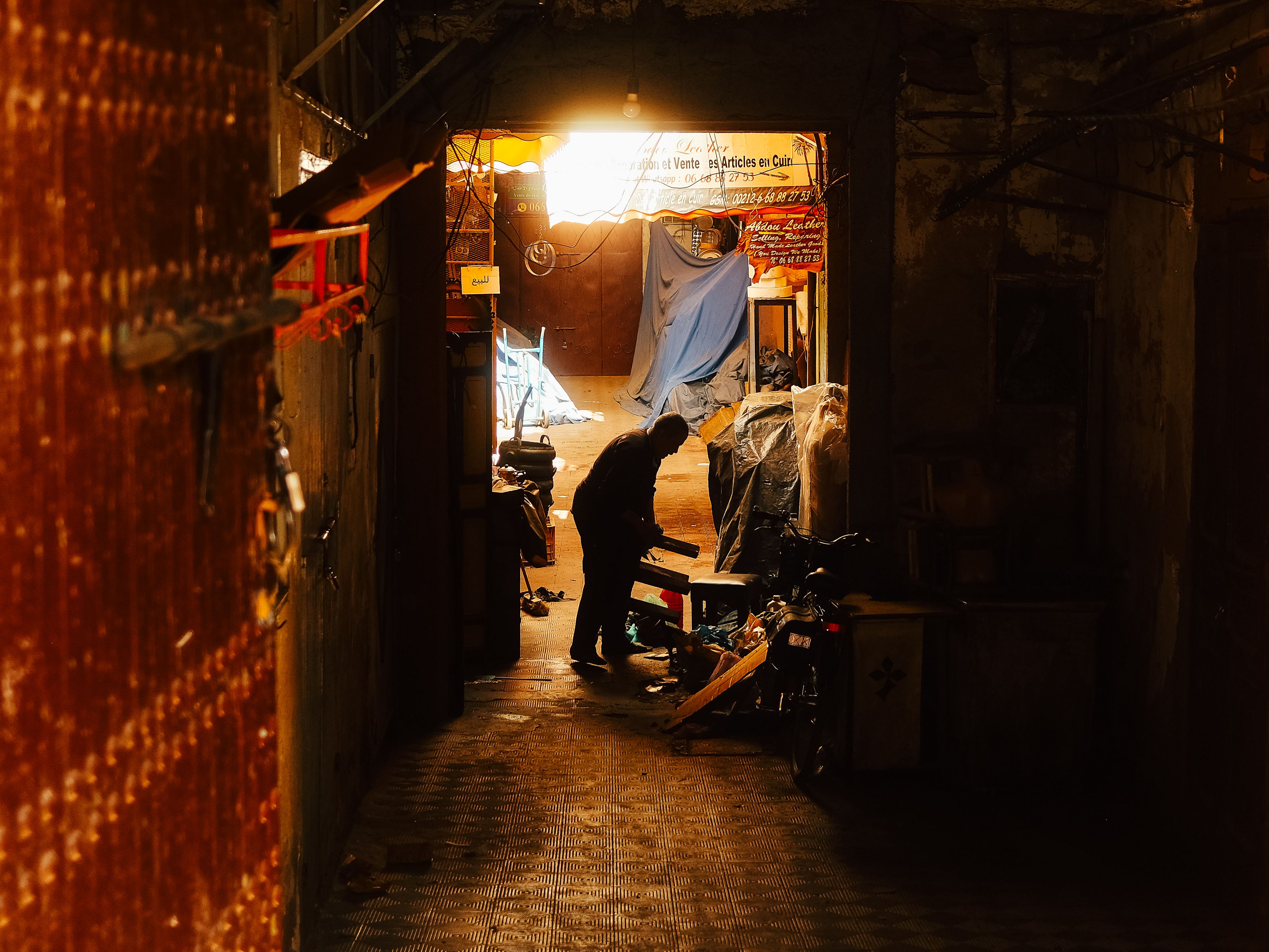 gratis Silhouet van een persoon die aan het werk is in een schemerig steegje. Warme tinten en een rustieke sfeer. Stockfoto