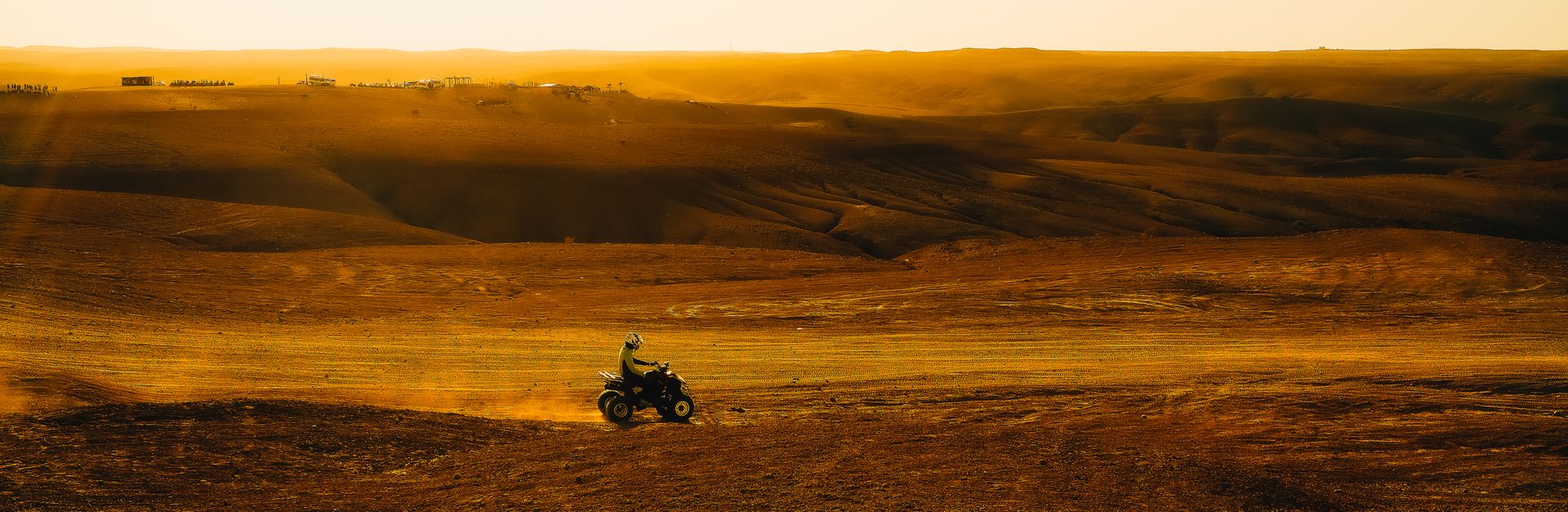 An ATV rider explores a wide open desert under a golden sunset, showcasing adventure and thrill.