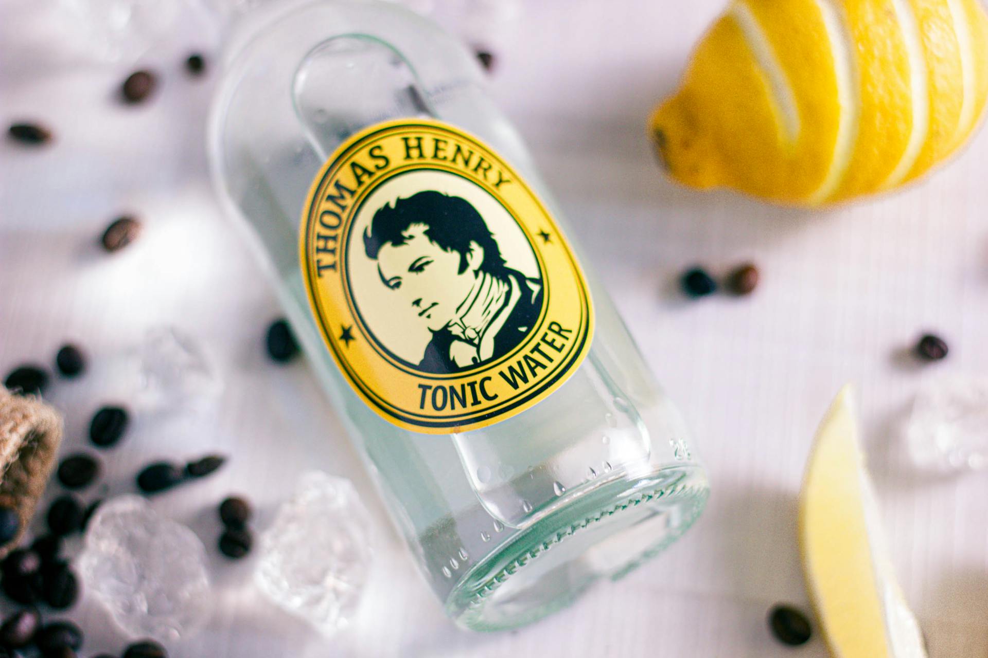 Close-up of Thomas Henry tonic water bottle with fresh lemon and ice cubes.