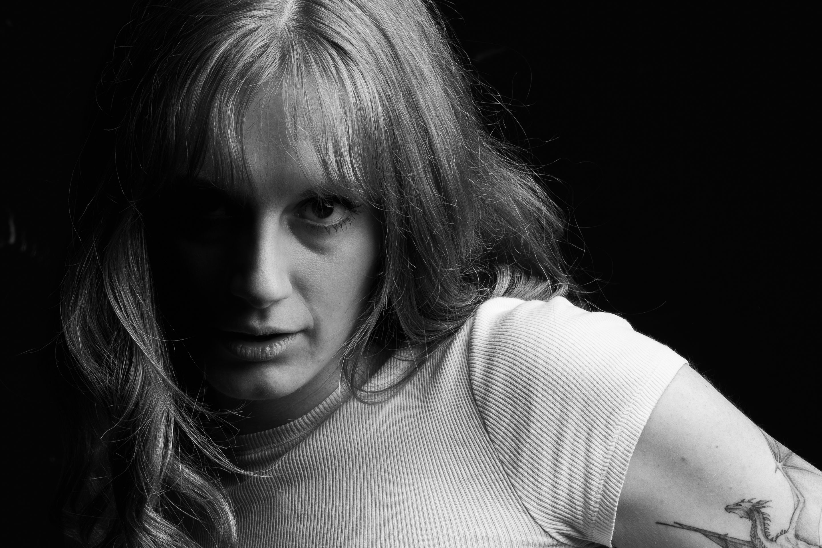 Intense black and white portrait of a woman with red hair and tattoos, exuding a seductive and mysterious vibe.