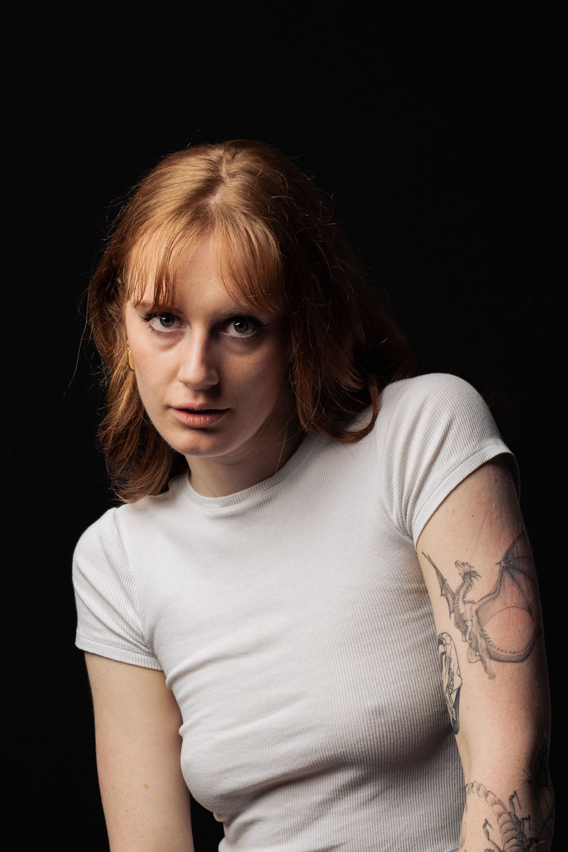Close-up portrait of a woman with tattoos and red hair against a dark background.