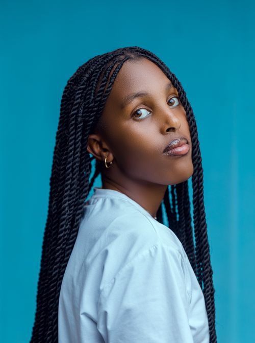 Free Woman with long braided hair posing against a bright blue background, exuding style and confidence. Stock Photo