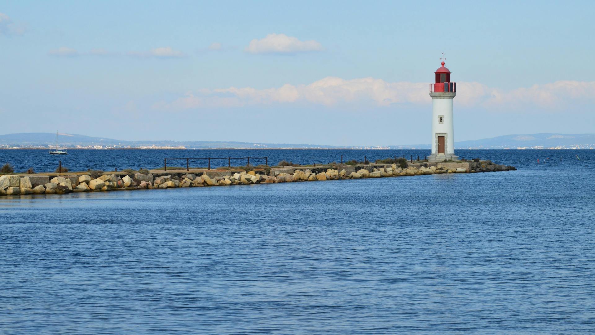 Peaceful view of a lighthouse and rocky jetty extending into the calm sea.
