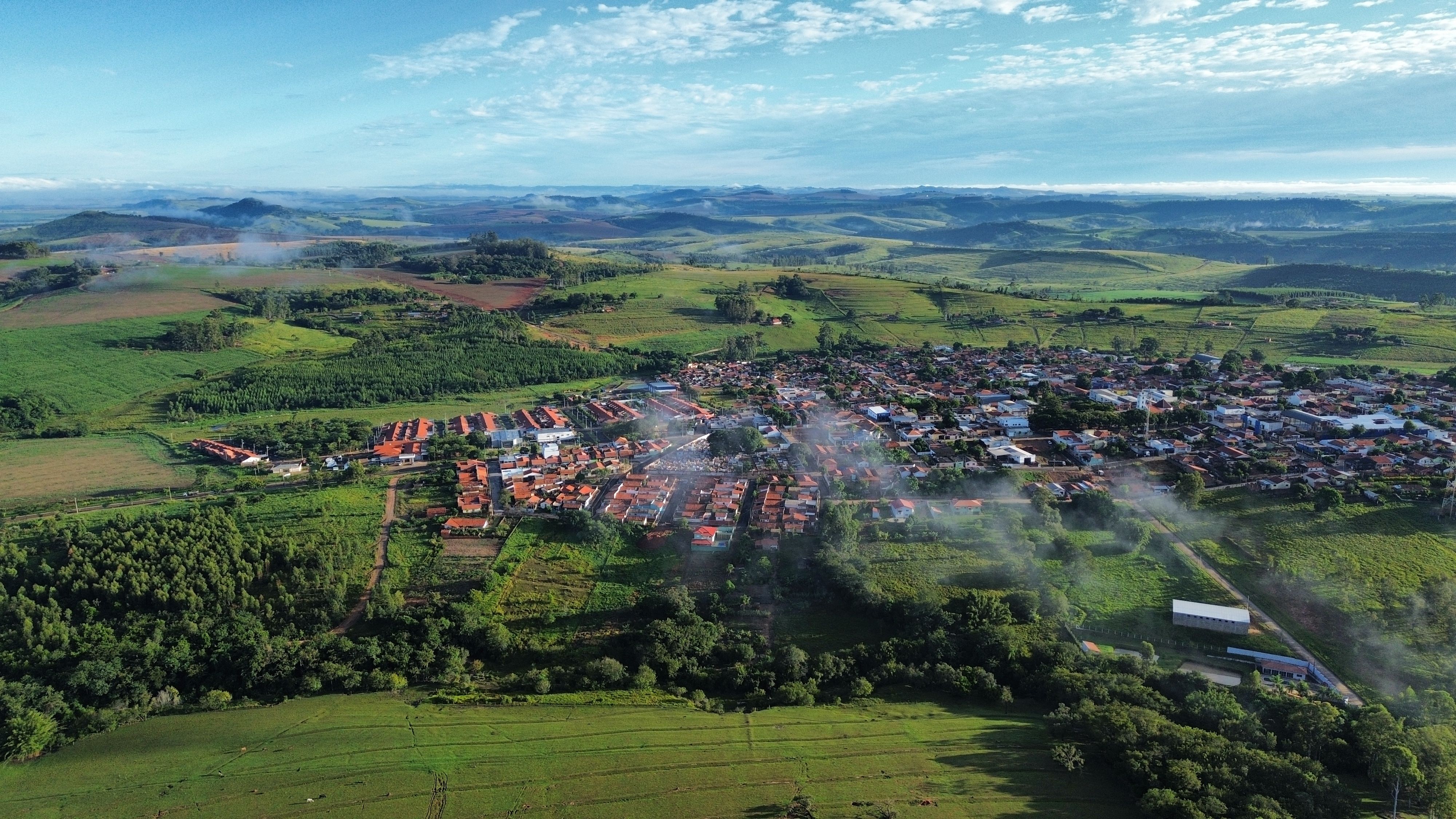 Aerial view of a village surrounded by lush greenery and hills under a clear sky.