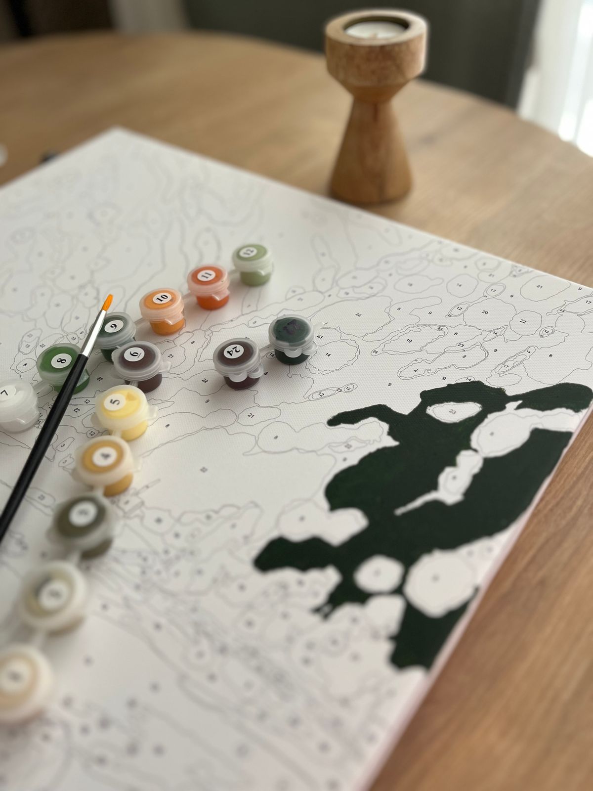 Paint by numbers kit with numbered canvas, brush, and paint pots on a wooden table