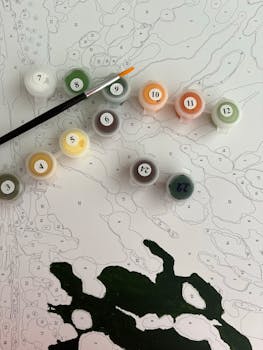 A paint-by-numbers set featuring paints and a brush laid on a detailed canvas.