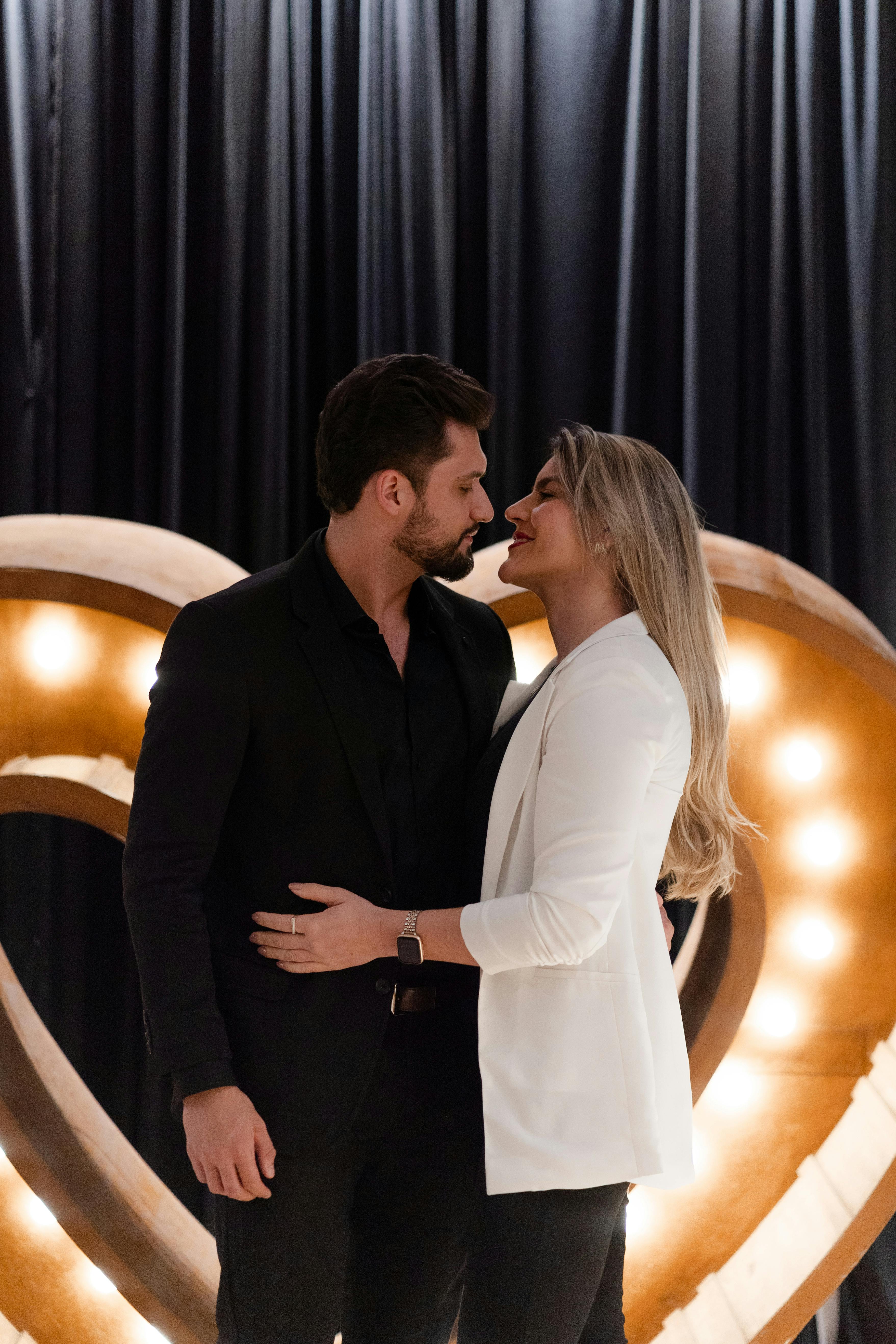 A couple sharing an intimate moment in front of illuminated heart decor.