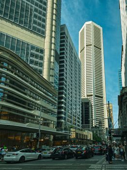 Dynamic city street hustle amid towering skyscrapers under blue sky.
