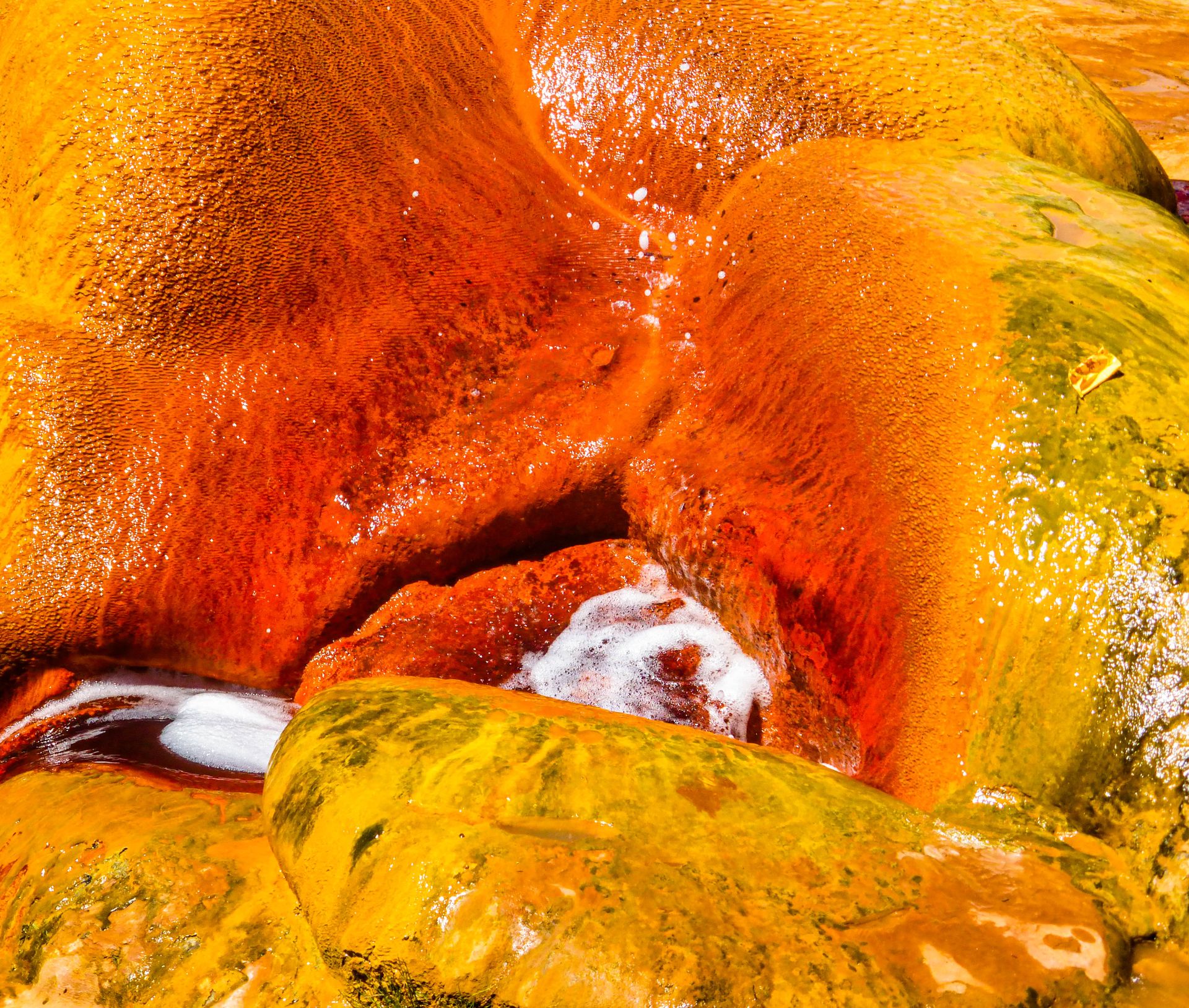 Close-up view of vivid orange and yellow geothermal deposits with flowing water.