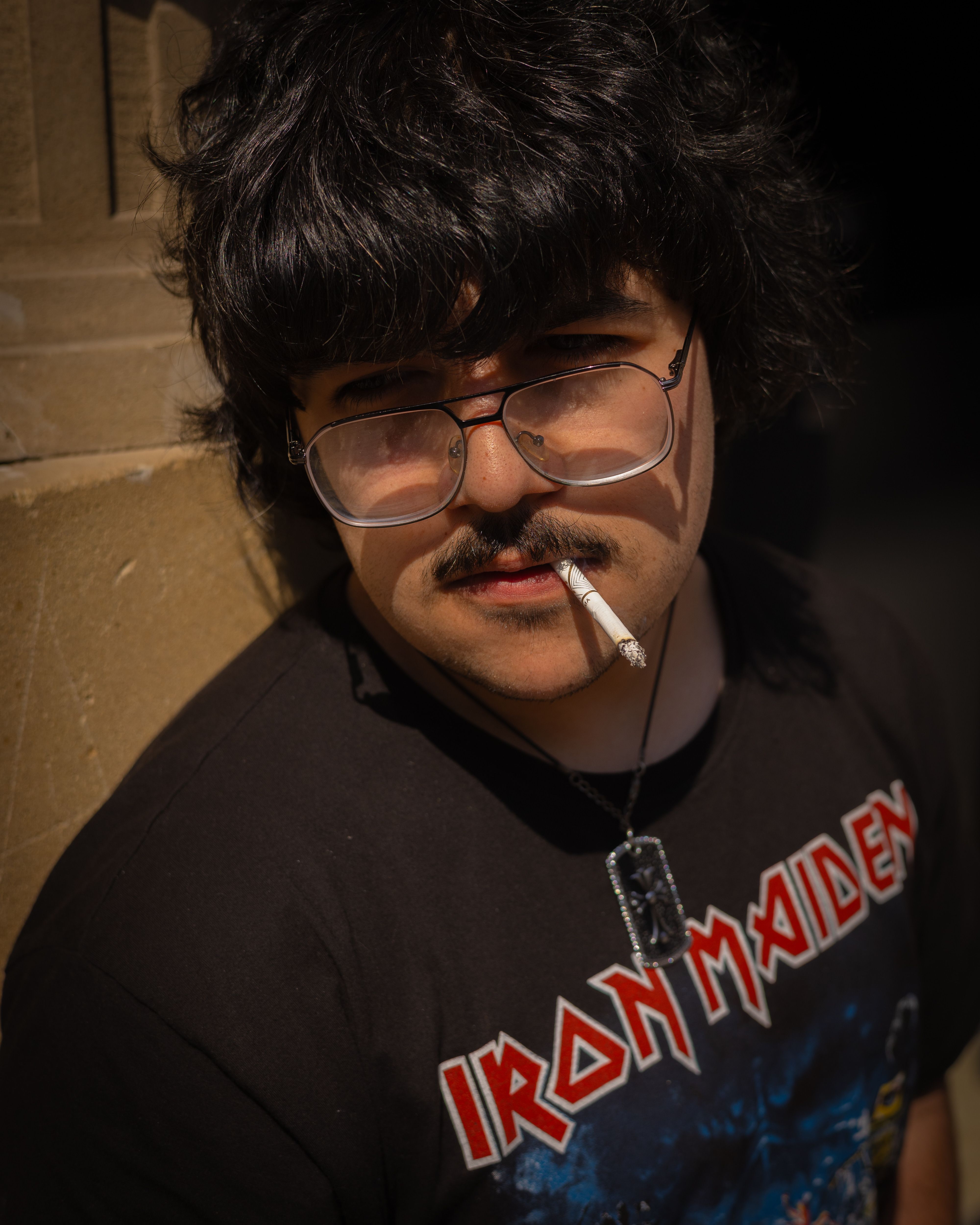 Portrait of a young man wearing glasses and a band shirt, smoking.