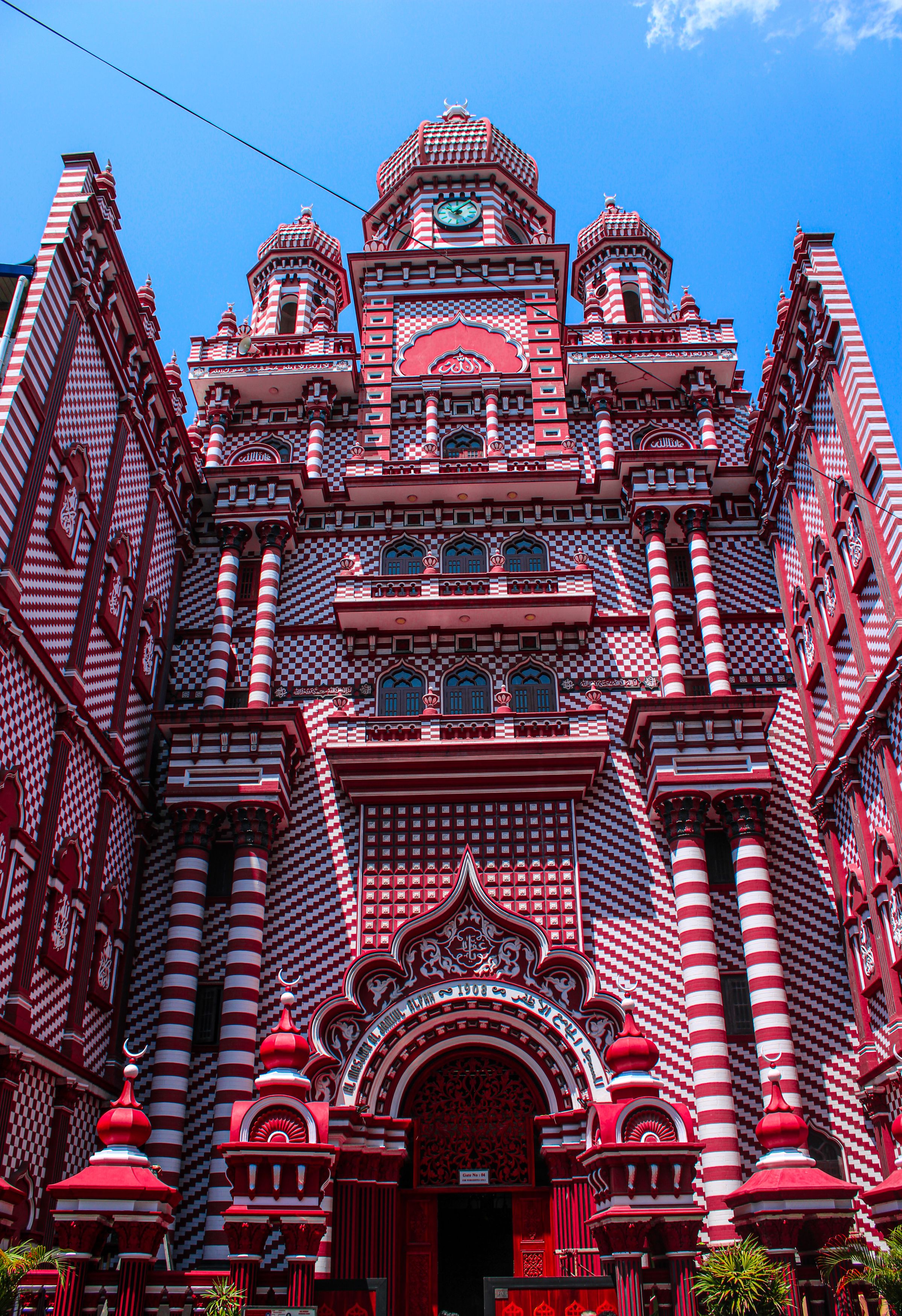 Striking red and white Jami Ul-Alfar Mosque in Colombo against a clear blue sky.