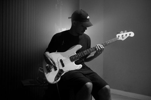 A musician plays a bass guitar in a dimly lit studio, creating a moody atmosphere.