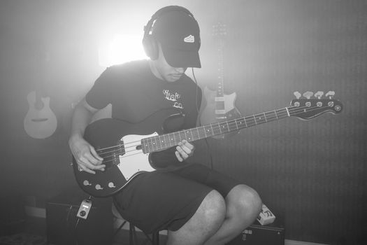 Musician plays electric bass guitar in studio, wearing headphones.