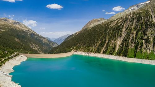 Free Stunning aerial shot of a dam and turquoise reservoir nestled in lush mountains. Stock Photo