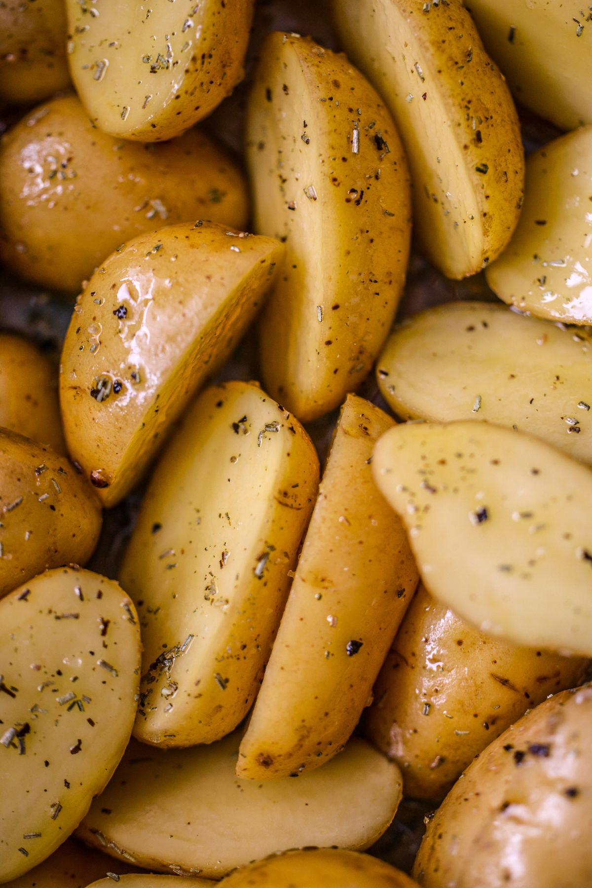 Raw potato halves seasoned with herbs and oil ready for roasting in the oven