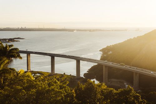 Free A stunning view of a sunlit bridge over a serene coastal landscape, ideal for travel imagery. Stock Photo