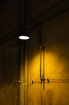 Moody urban scene with a dim street lamp casting light on a textured wall.
