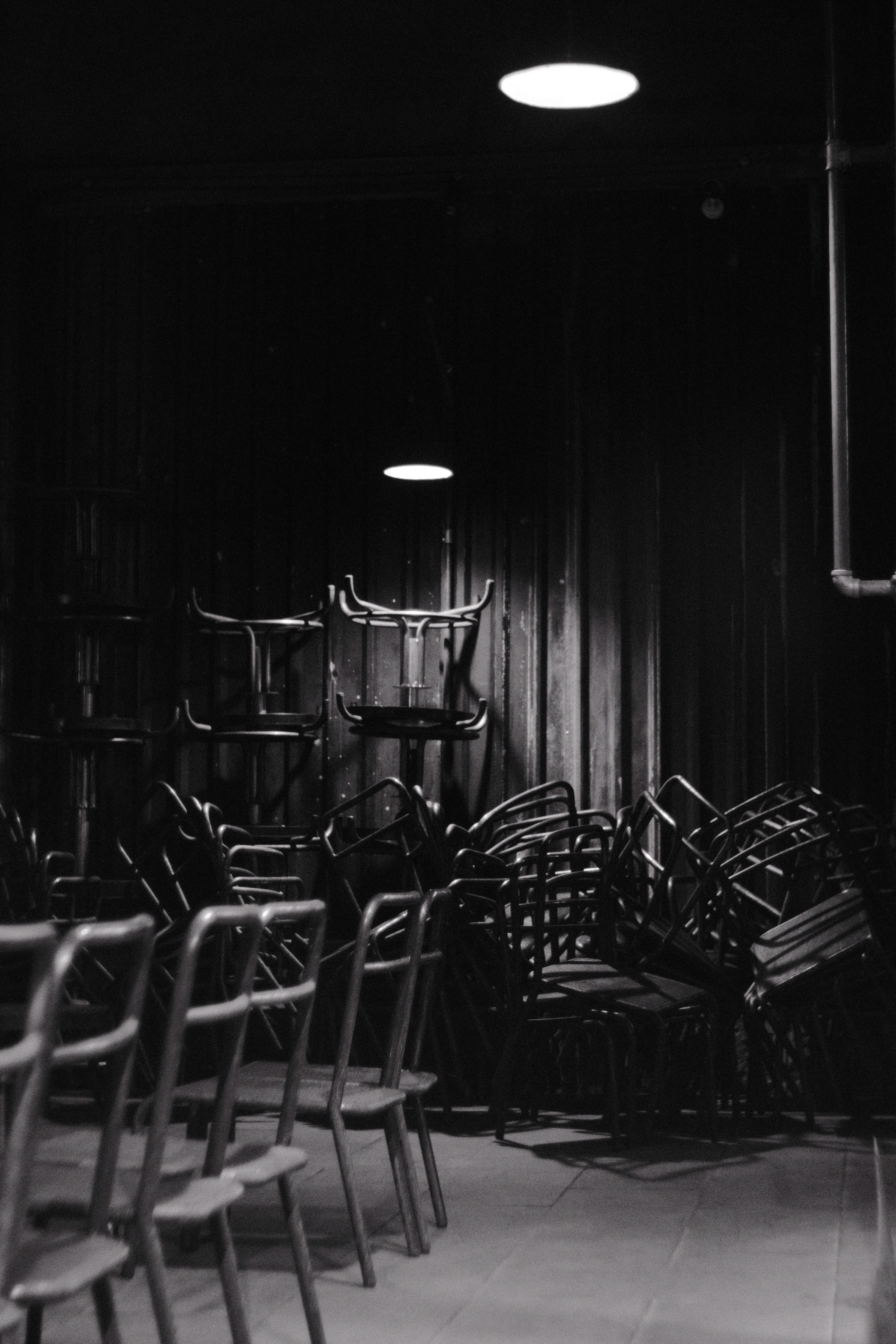 Ilmainen Tunnelmallinen mustavalkoinen valokuva pinotuista metallituoleista hämärässä huoneessa. Kuvapankkikuva