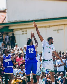 Players in blue and white jerseys compete in a lively outdoor basketball match.
