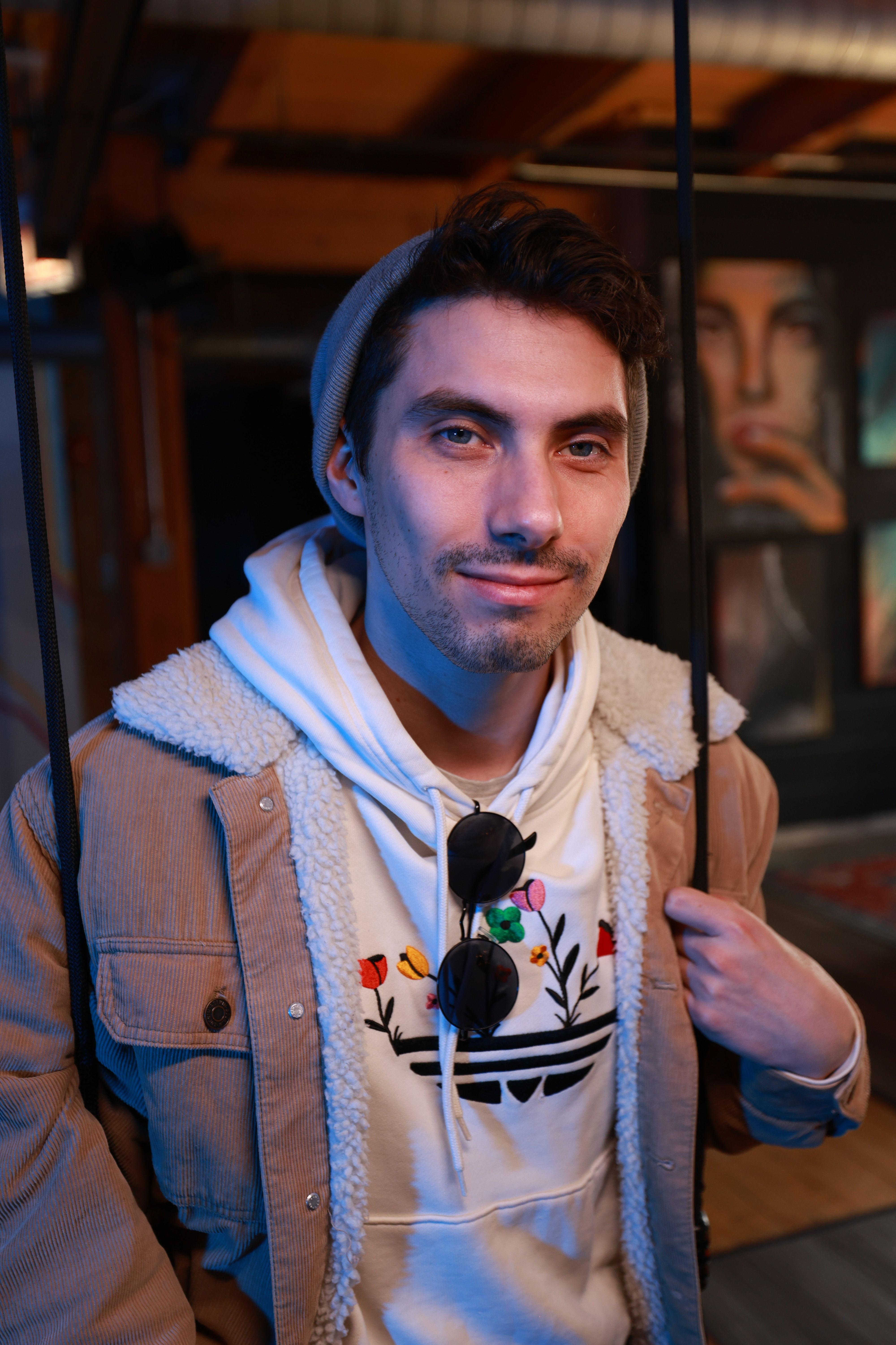Stylish young man in casual attire posing indoors with art in background.