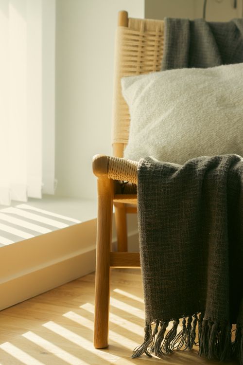 Free A simple wicker chair draped with a blanket in a sunlit room, conveying a cozy minimalist aesthetic. Stock Photo