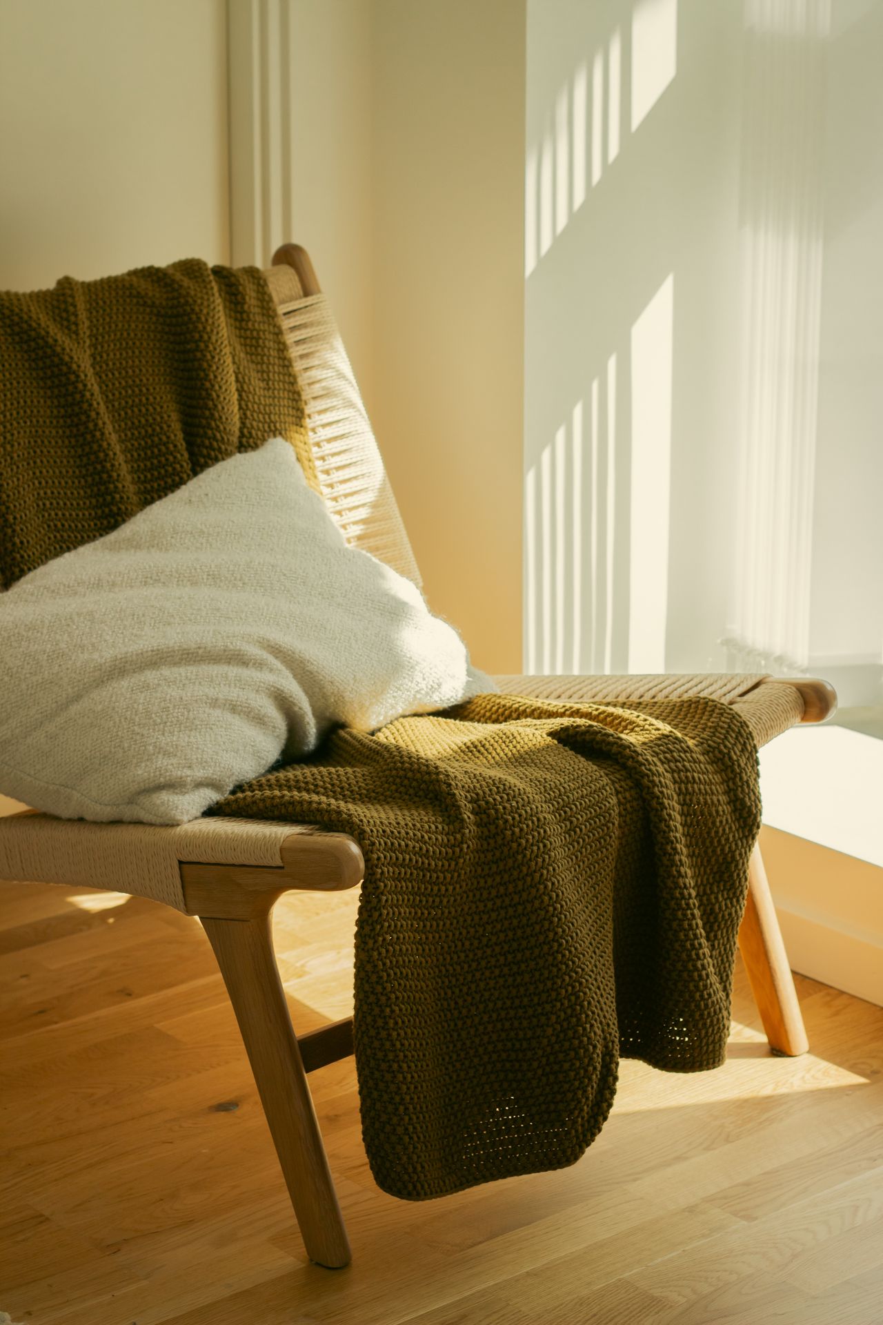 Green knit throw draped over a wooden chair in sunlight