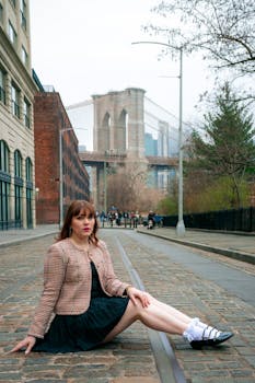 Stylish woman posing in New York with Brooklyn Bridge in the background.