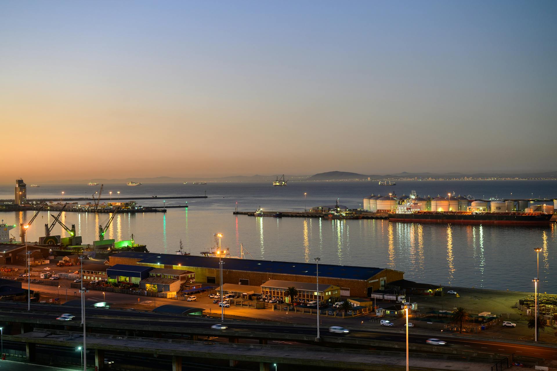 A stunning twilight view of a bustling harbor in Cape Town with illuminated docks and calm waters.