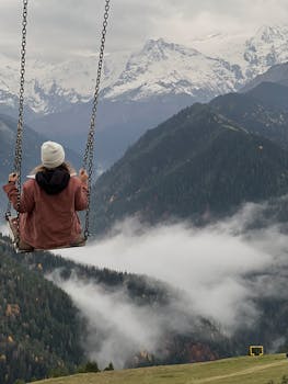 Person on swing enjoys breathtaking view of snowy mountains in serene landscape.