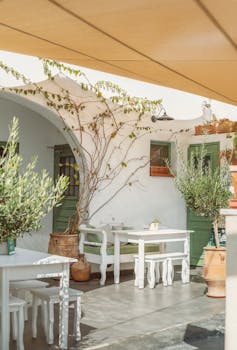 Quaint outdoor cafe setting in Fira, Greece with white furniture and vibrant greenery.