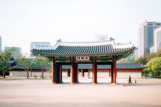 Historic Korean gate amidst urban Seoul skyscrapers under a bright sky.