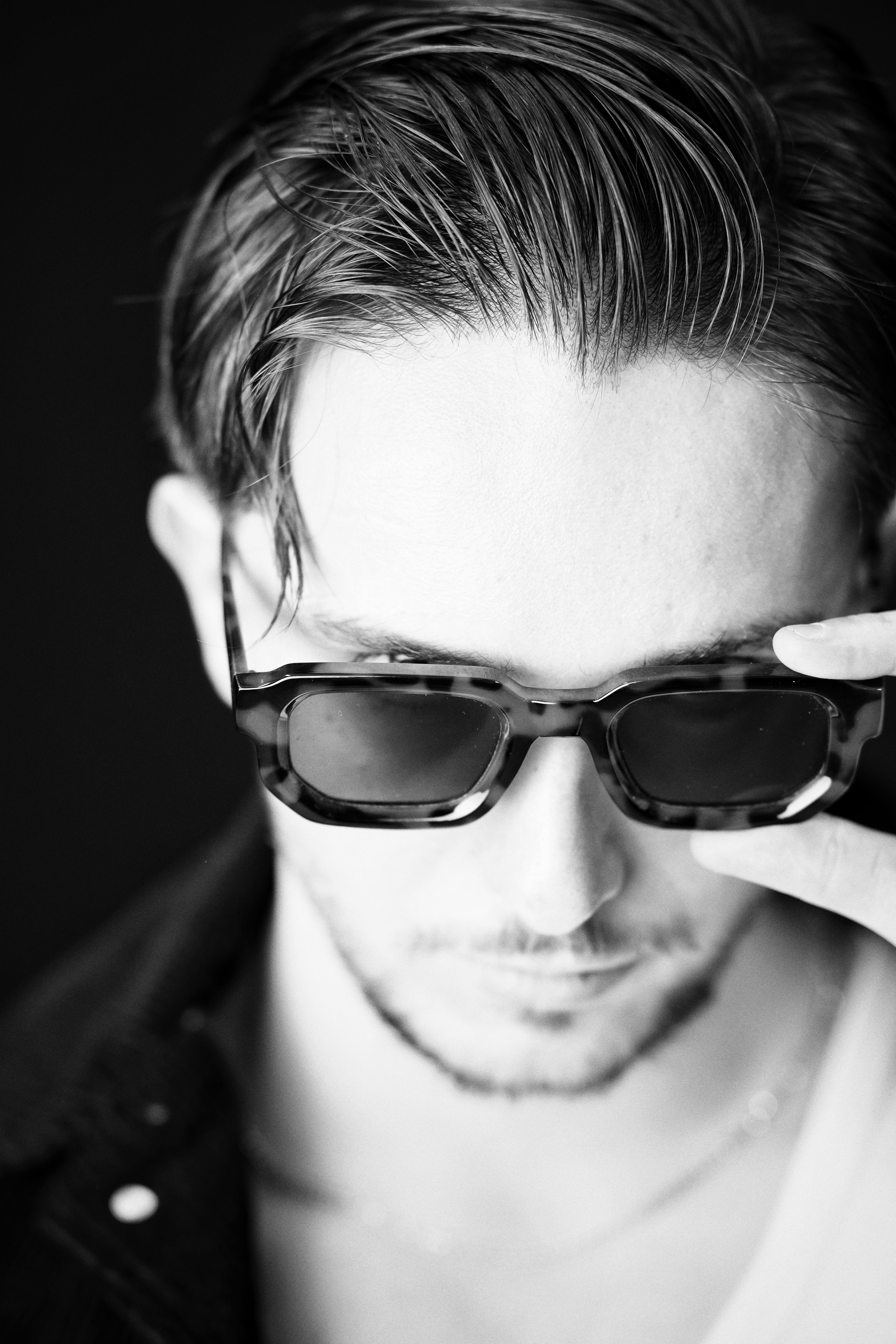Free Black and white portrait of a man adjusting sunglasses, exuding style and mystery. Stock Photo