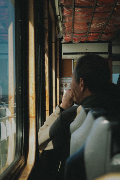 Free Man gazing out of a moving train's window, bathed in sunlight, evoking solitude. Stock Photo