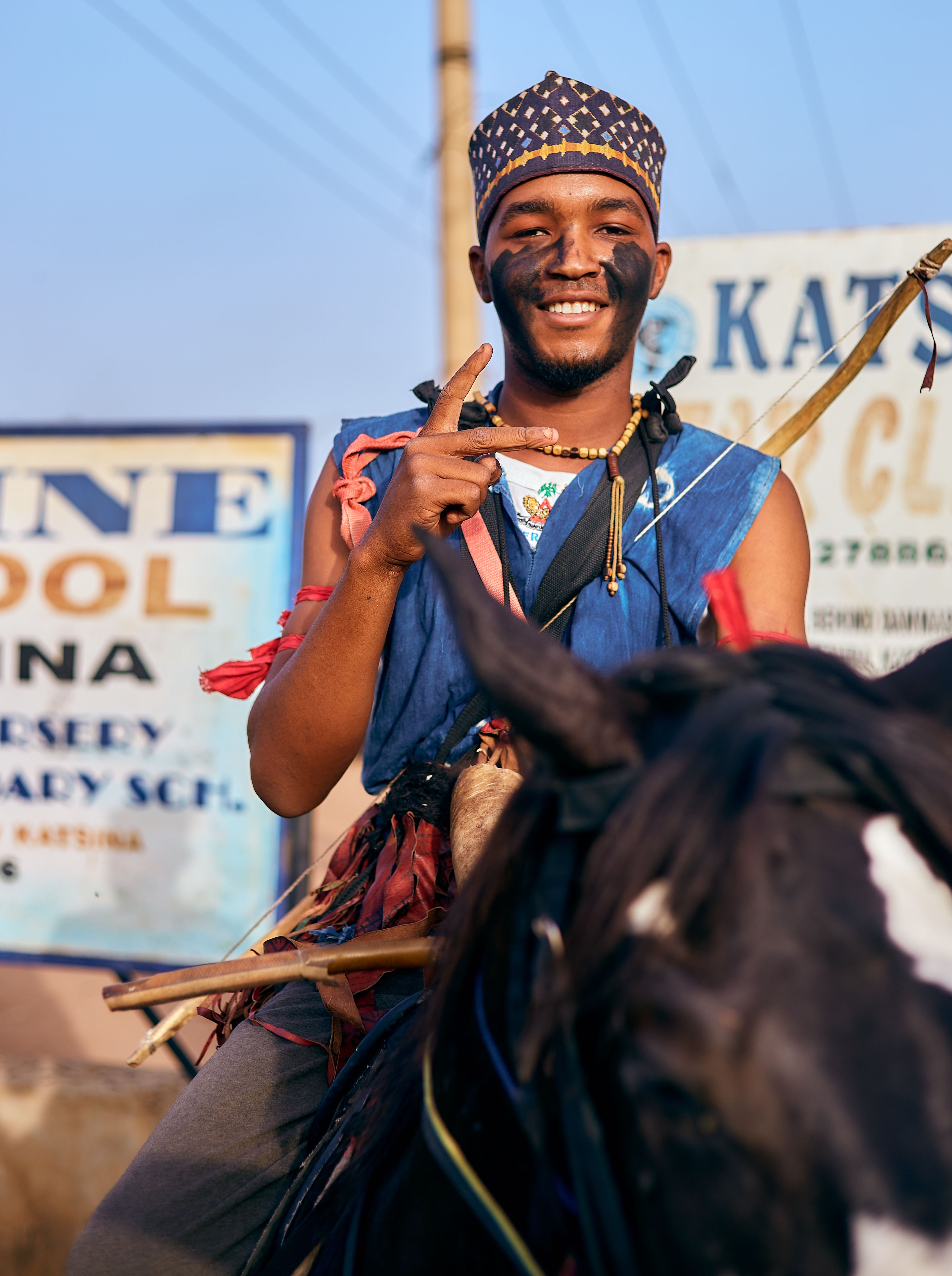 Smiling young man celebrates on horseback during a vibrant cultural festival outdoors.