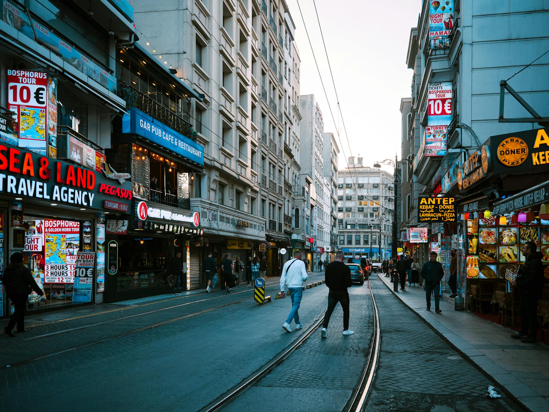Vibrant street scene in Istanbul featuring shops, people, and tram tracks under a clear sky.