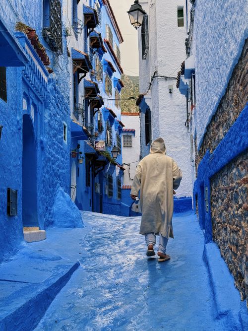 Free A person in traditional attire walks through Chefchaouen's iconic blue streets. Stock Photo