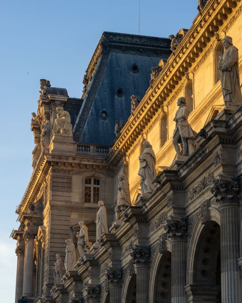 Free Elegant sunlit facade of the iconic Louvre Museum with classical sculptures in Paris, France. Stock Photo