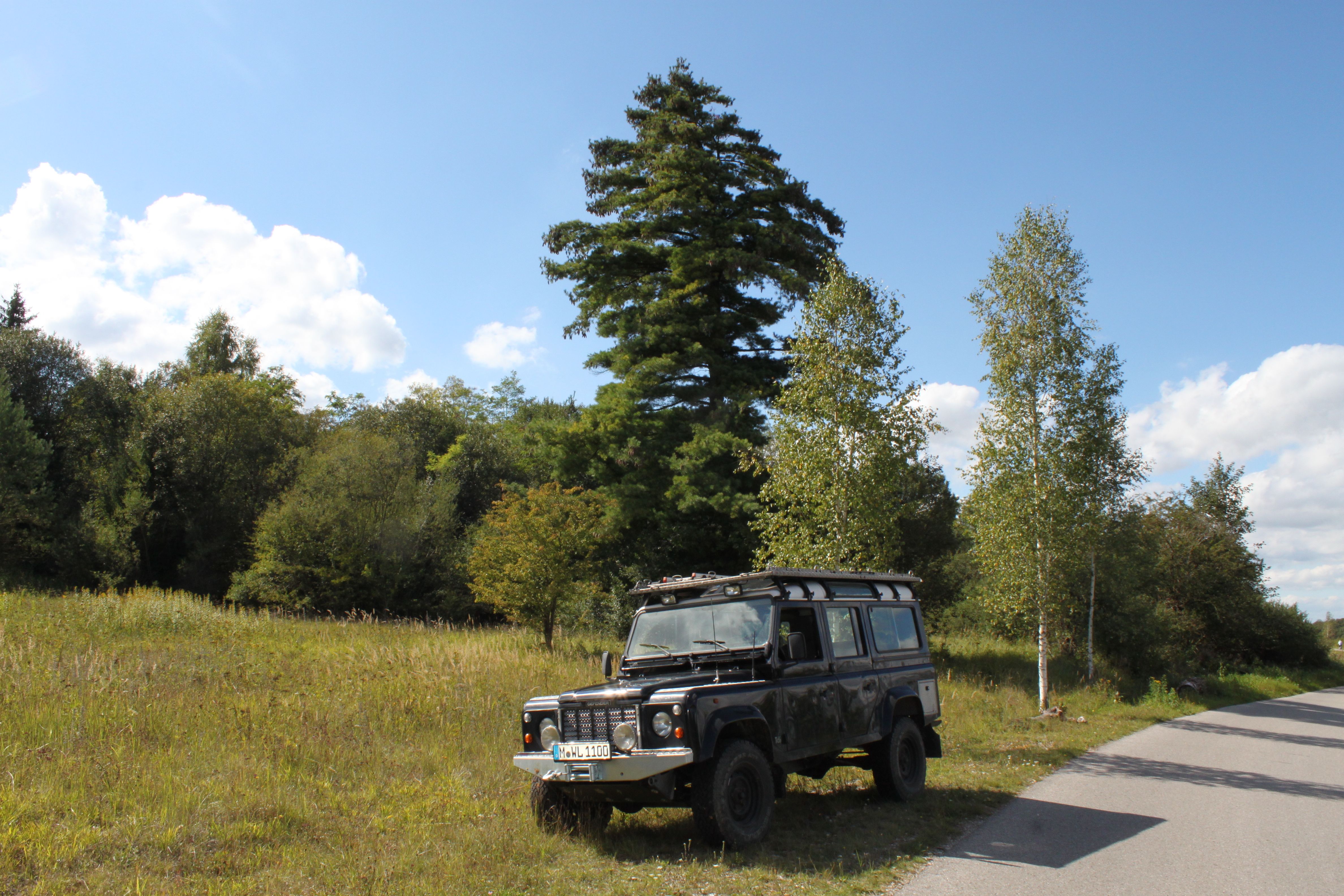 Fotomural Land Rover clásico estacionado en un pintoresco paisaje rural bajo un cielo soleado.