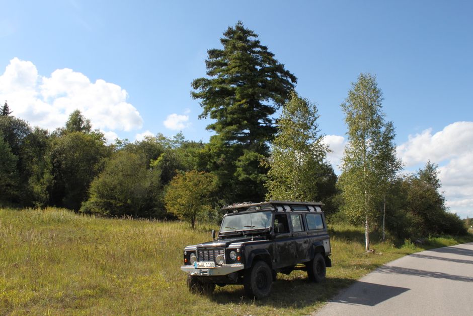 Fotomural Land Rover clásico estacionado en un pintoresco paisaje rural bajo un cielo soleado.