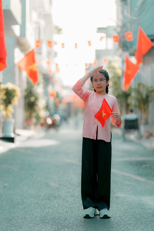 Free A girl in pink outfit stands on a street holding a Vietnamese flag with decorations. Stock Photo