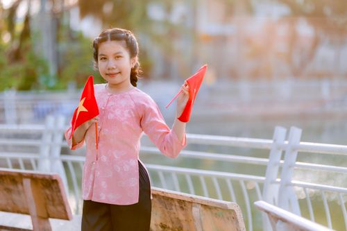 Free Young girl holding flags outdoors, smiling in soft warm daylight, wearing traditional attire. Stock Photo