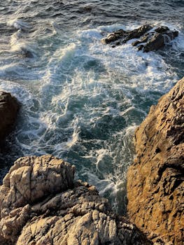 The waves crash against rocky cliffs at Point Lobos, capturing dramatic ocean energy.